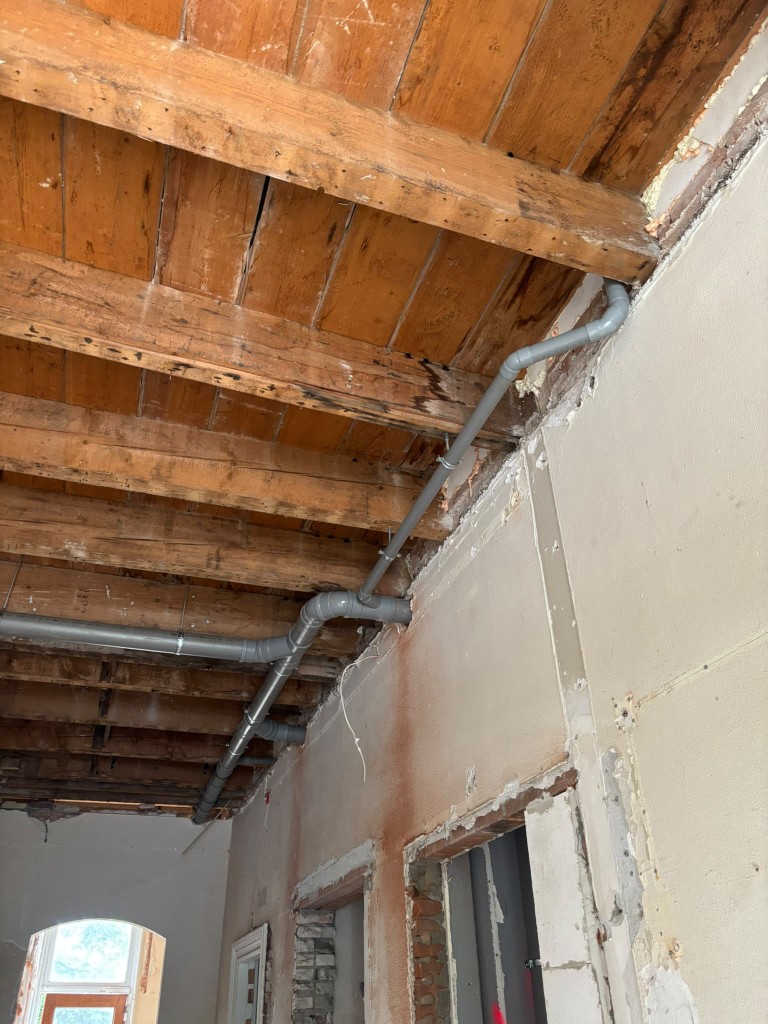 Grijze afvoerleidingen langs de balken van een plafond, tijdens een verbouwing.